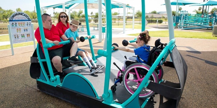 children and adults using inclusive play equipment