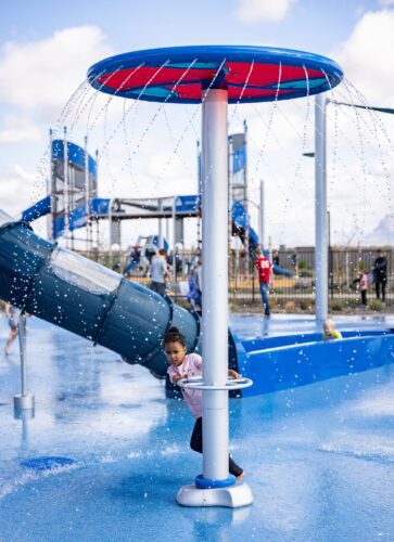 Children spinning a water sprayer at a colorful splash pad