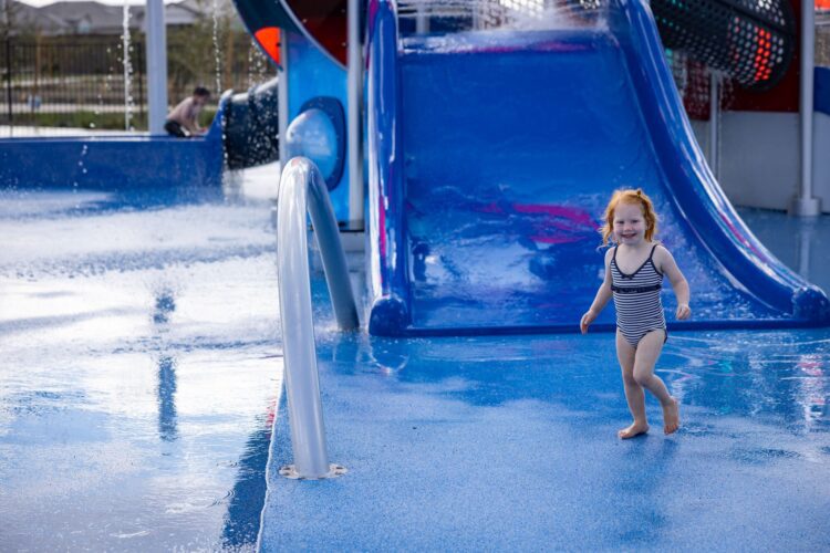 Child playing at a colorful splash pad with slides and sprayers in Apache Junction, AZ