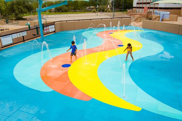 Children splashing in outdoor water playground with multiple fountains
