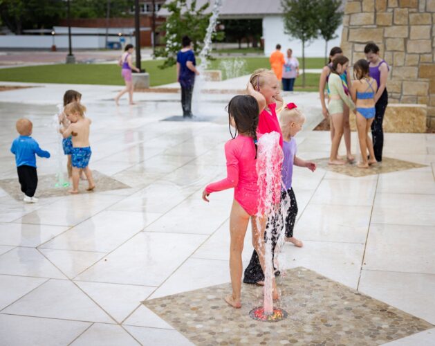 Children play at a splash pad at District 1876, Coleman, Texas.