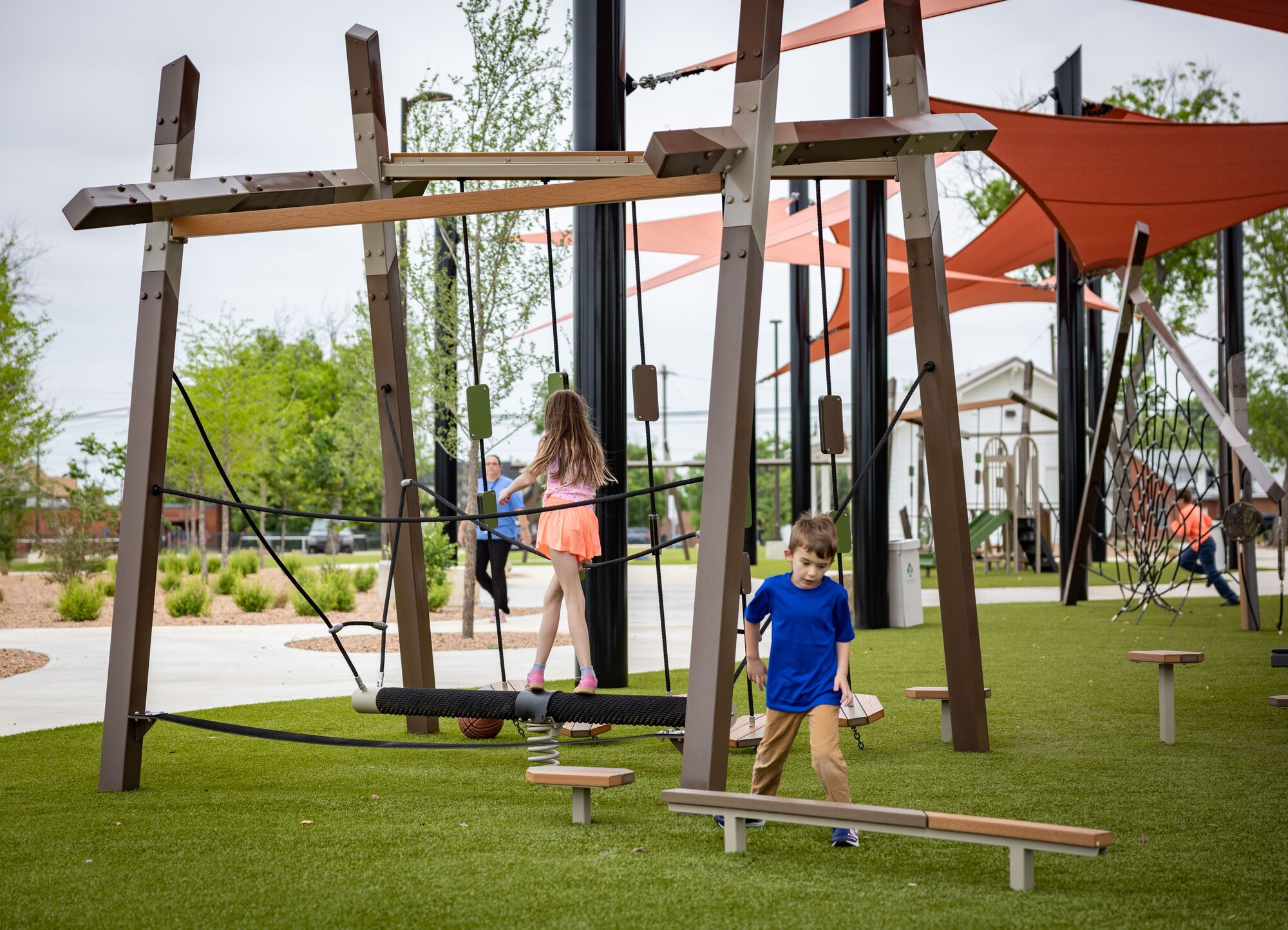 Children playing at a playground under red shade sails at District 1876, Coleman, Texas.