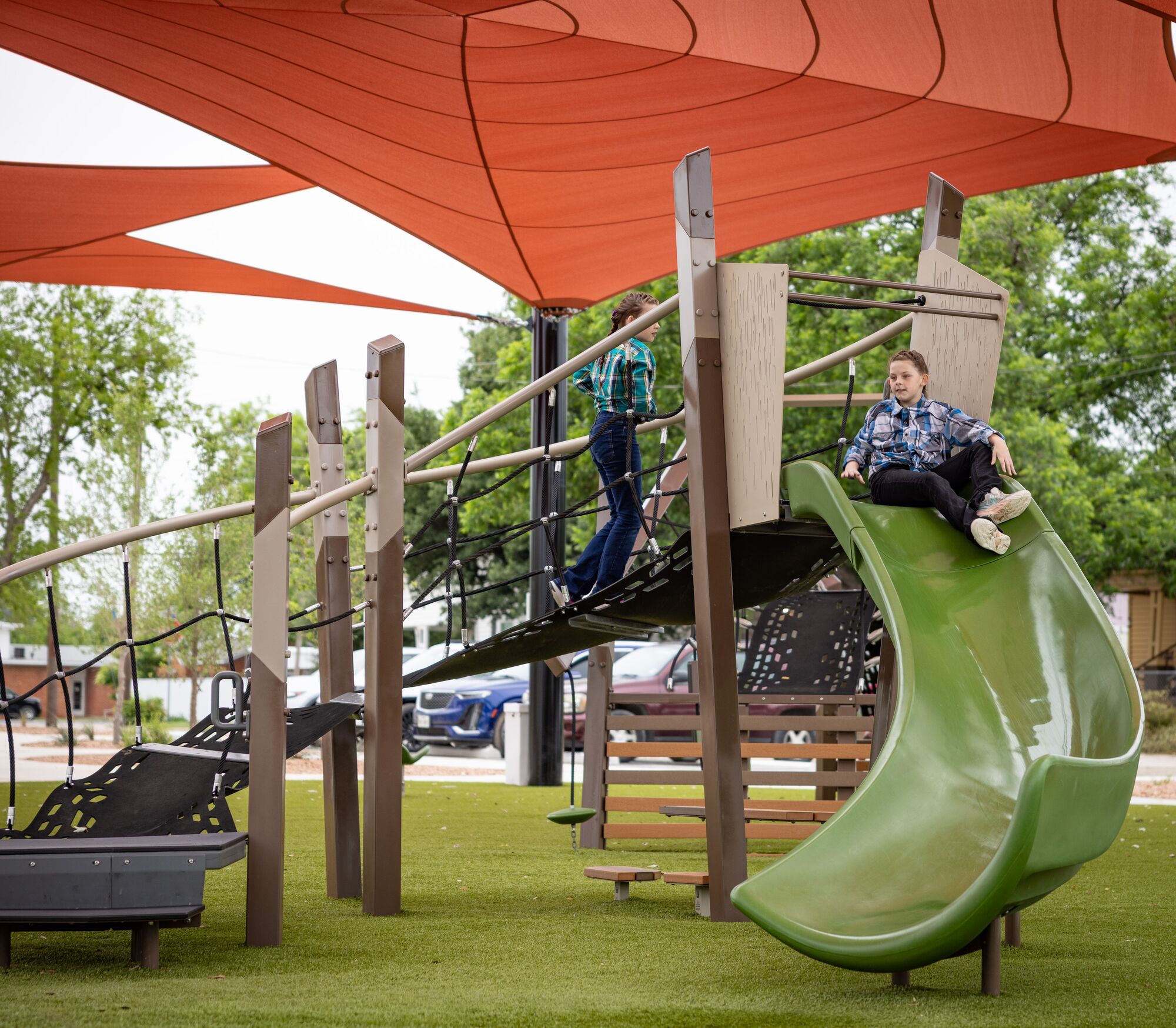 Child riding a slide at playground under red shade sails at District 1876, Coleman, Texas.
