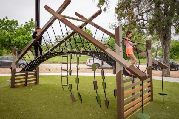 Children playing at a playground under red shade sails at District 1876, Coleman, Texas.