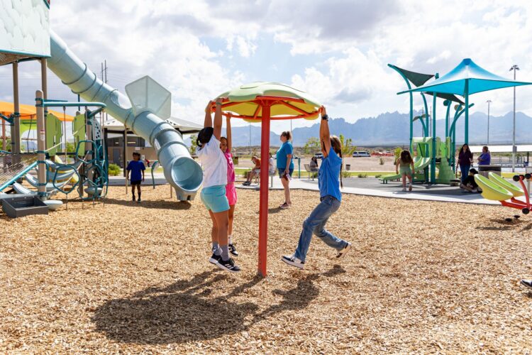 Children laugh and spin on colorful playground spinner at East Mesa Public Recreation Complex, in Las Cruces, New Mexico