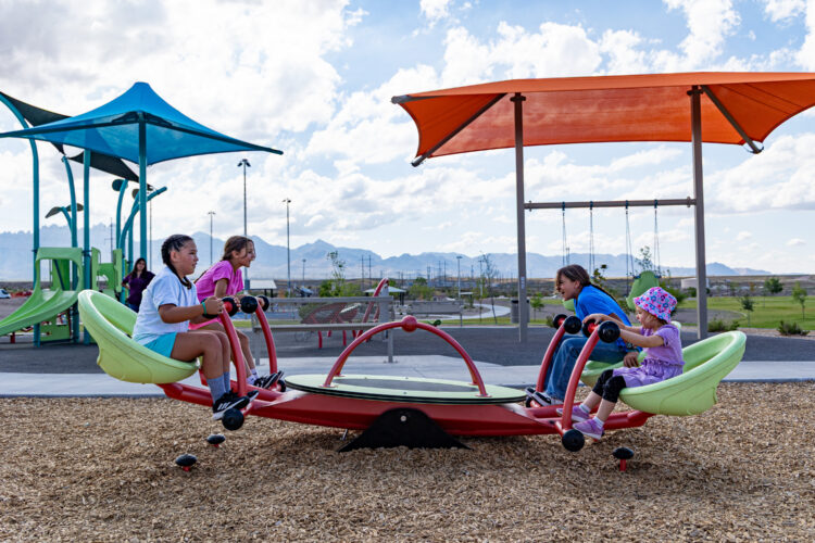 Children play at colorful playground with four person seesaw at East Mesa Public Recreation Complex, in Las Cruces, New Mexico