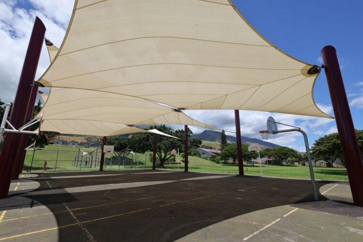 Kids playing under commercial playground shade on a sunny afternoon in Lahaina, Hawaii