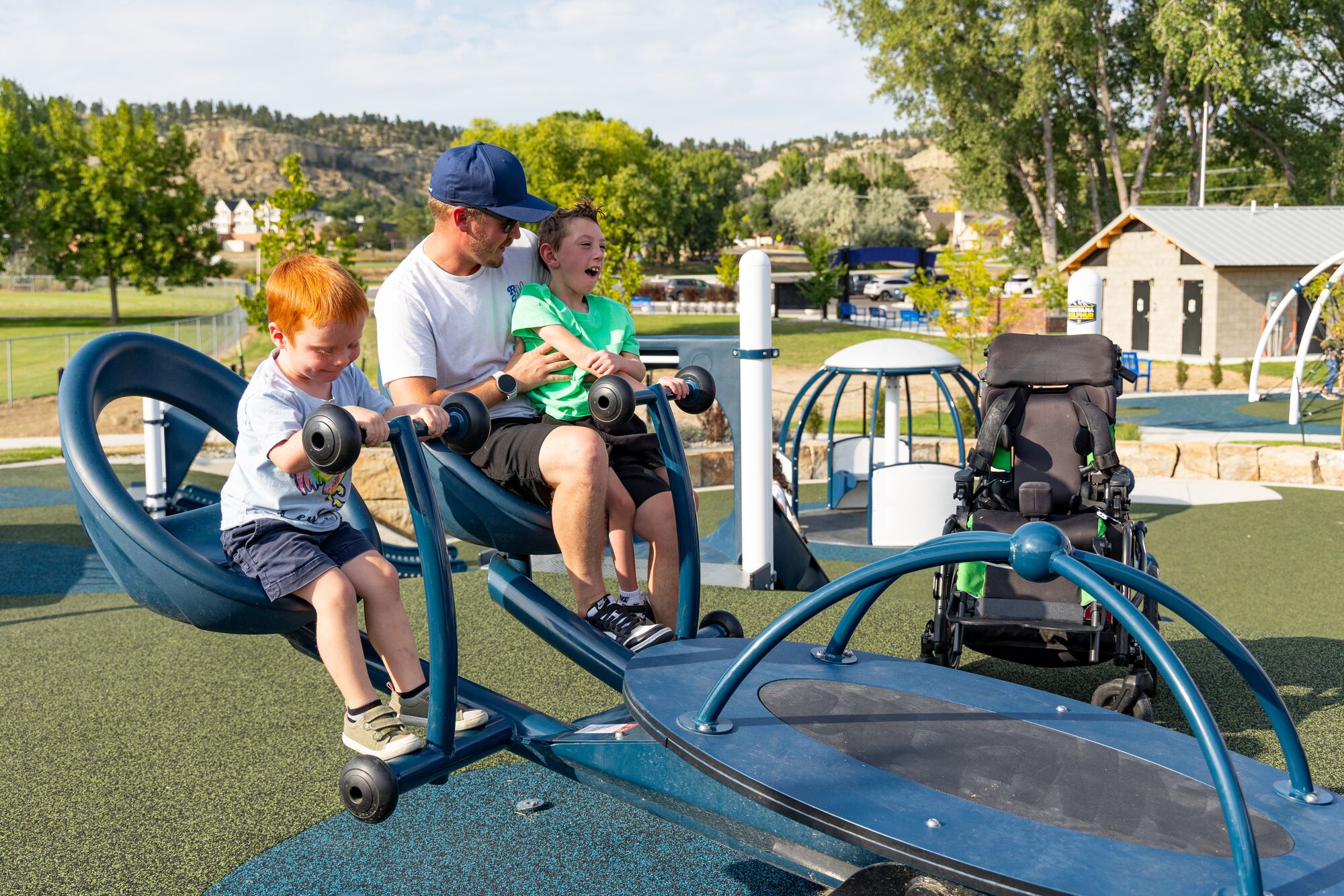 Child and caregiver play on inclusive four person seesaw